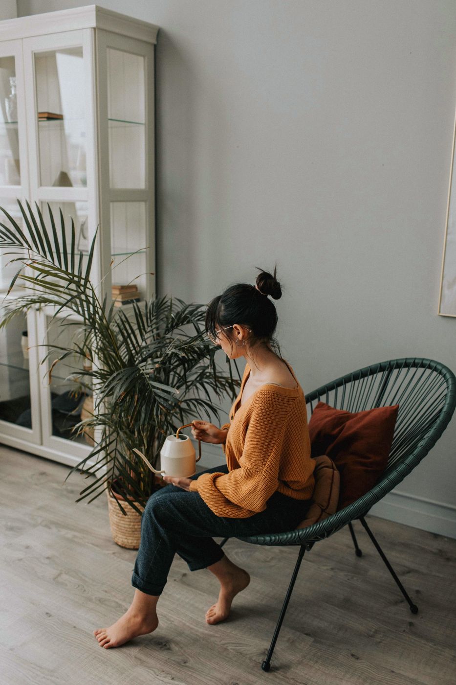 A woman sitting in a chair at home beside a plant